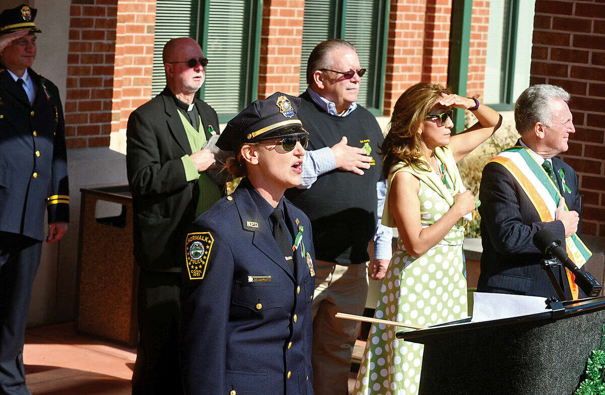 Hour photo / Erik Trautmann Norwalk police detective Kristina Lapak sings The National Anthem as the Norwalk Police Department Emerald League holds a ceremony in front of police headquarters before the first St. Patrick's Day parade Thursday.