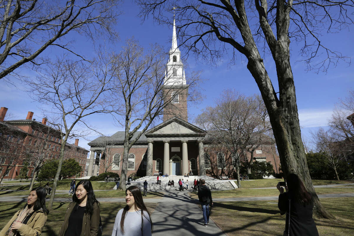 In this Sunday, March 13, 2016, photo people walk near Memorial Church, behind, on the campus of Harvard University, in Cambridge, Mass. Amid scrutiny from Congress and campus activists, colleges across the country are under growing pressure to reveal the financial investments made using their endowments. (AP Photo/Steven Senne)