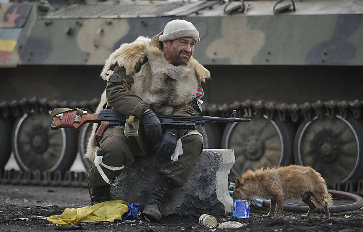 A Russia-backed rebel rests as a dog eats from a can in Debaltseve, Ukraine, Friday, Feb. 20, 2015. After weeks of relentless fighting, the embattled Ukrainian rail hub of Debaltseve fell Wednesday to Russia-backed separatists, who hoisted a flag in triumph over the town. The Ukrainian president confirmed that he had ordered troops to pull out and the rebels reported taking hundreds of soldiers captive.(AP Photo/Vadim Ghirda)