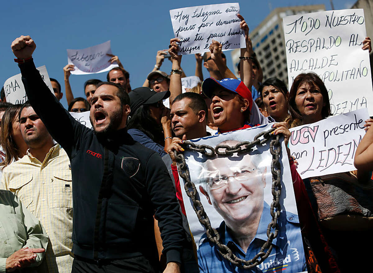A supporter of Caracas Mayor Antonio Ledezma holds a poster of him with chains during a protest demanding his release in Caracas, Venezuela, Friday, Feb. 20, 2015. Demonstrators are condemning last night's surprise arrest of Ledezma for allegedly plotting to overthrow the government of President Nicolas Maduro. Late Thursday Maduro said Ledezma, one of the most vocal opposition leaders, would be punished for trying to sow unrest in Venezuela. (AP Photo/Alejandro Cegarra)
