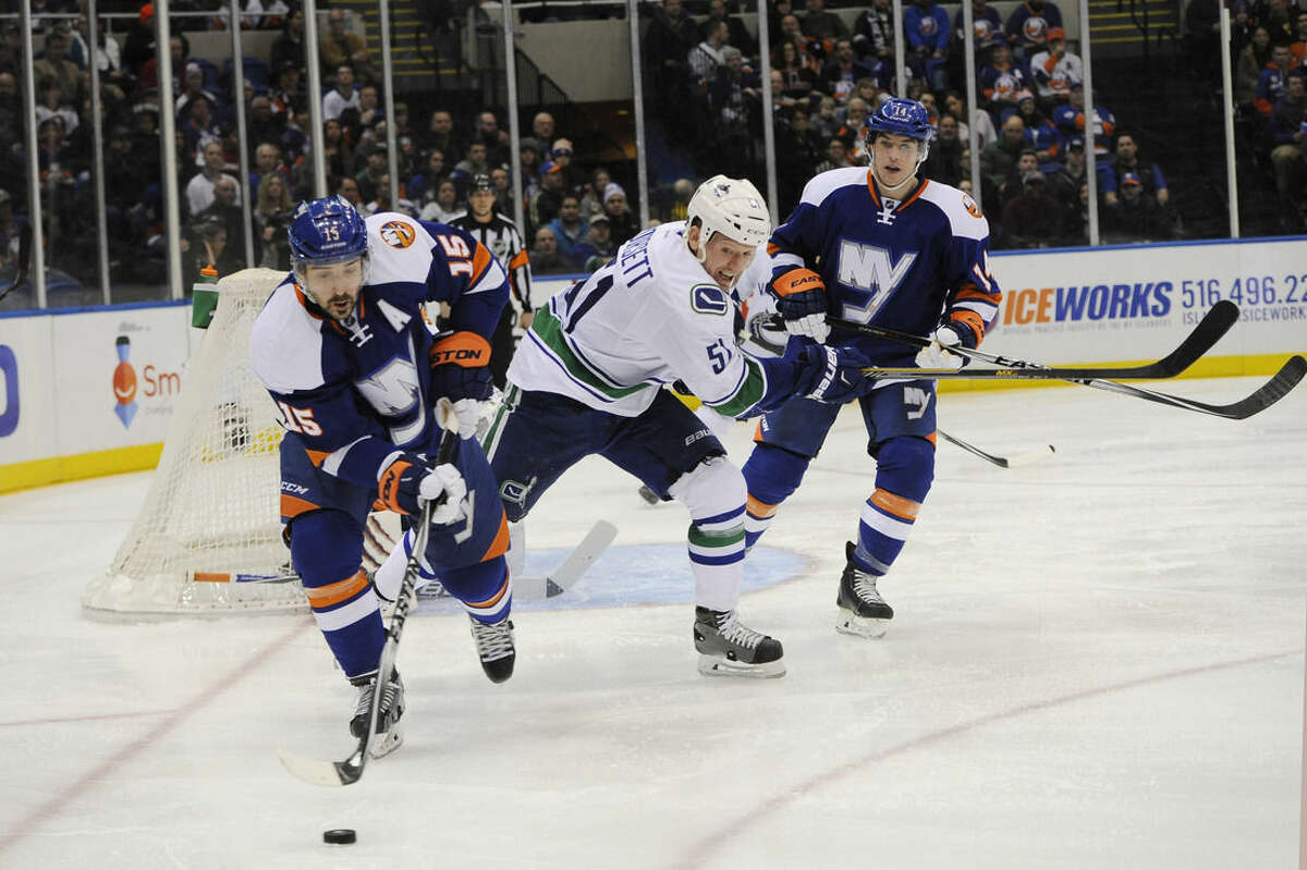 New York Islanders right wing Cal Clutterbuck (15) drives the puck away from Vancouver Canucks right wing Derek Dorsett (51) as Islanders defenseman Thomas Hickey (14) defends in the first period of an NHL hockey game at Nassau Coliseum on Sunday, Feb. 22, 2015, in Uniondale, N.Y. (AP Photo/Kathy Kmonicek)