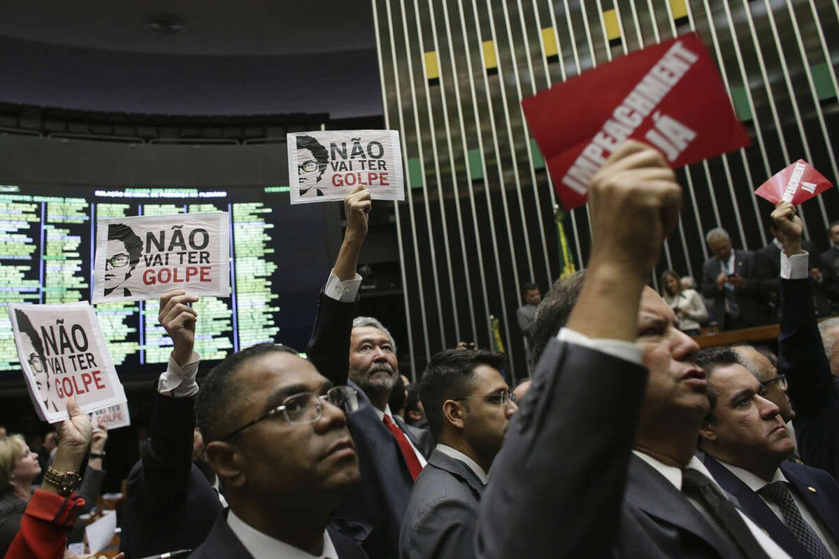 Opposition lawmakers, right, hold up placards with a message that reads in Portuguese; "Impeachment Now", while standing behind them are pro-government legislators holding sheets of paper printed with images of Brazil's President Dilma Rousseff and the message,"There will be no coup", during the formation of a committee on whether to begin impeachment proceedings against Rousseff, in Brazil's lower house, in Brasilia, Thursday, March 17, 2016. (AP Photo/Eraldo Peres)