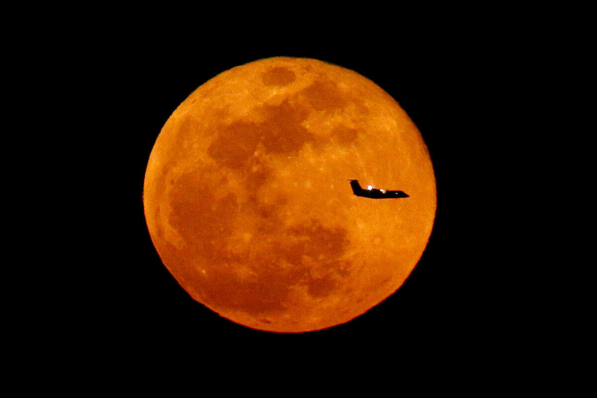 A plane descending into Newark Liberty International Airport crosses over the full moon rising seen from Eagle Rock Reservation, Wednesday, March 23, 2016, in West Orange, N.J. (AP Photo/Julio Cortez)