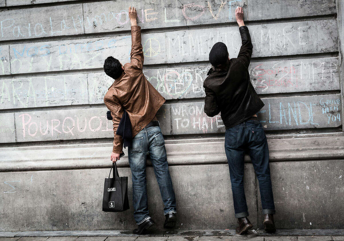 Two men write on a wall at a memorial for victims of attacks in Brussels on Wednesday, March 23, 2016. Belgian authorities were searching Wednesday for a top suspect in the country's deadliest attacks in decades, as the European Union's capital awoke under guard and with limited public transport after scores were killed and injured in bombings on the Brussels airport and a subway station. (AP Photo/Valentin Bianchi)