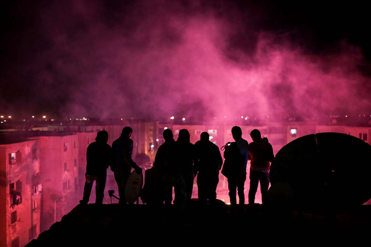 In this Thursday, March 5, 2015 photo, young men observe from a rooftop as smoke from flares fills the sky during a local wedding in Salam City, a suburb on the outskirts of Cairo. Since the 2011 uprising, the music of "Mahraganat," Arabic for "festivals," has emerged from and spread through impoverished communities, where local musicians play, especially during weddings, their auto-tuned beats and songs that tackle social, political and cultural issues. (AP Photo/Mosa'ab Elshamy)