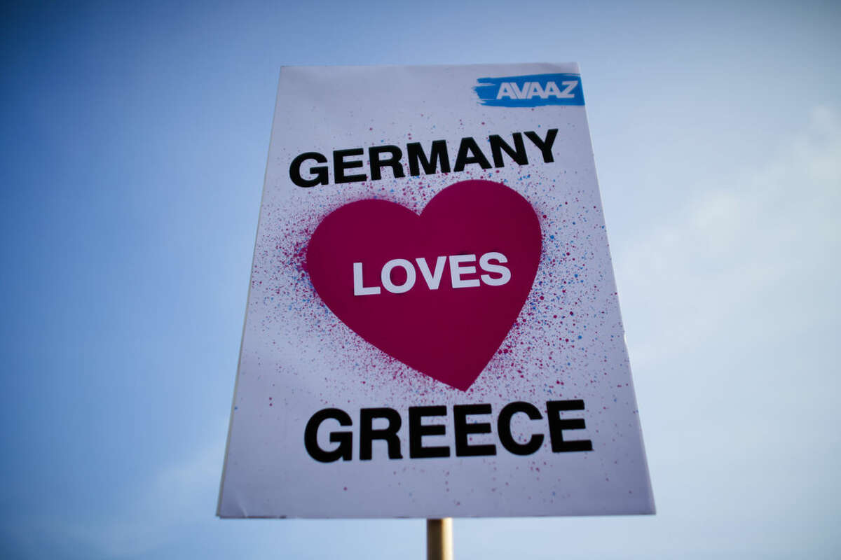 A protestor of the Avaaz organization holds up a poster during a demonstration for German-Greek solidarity prior to a bilateral meeting of German Chancellor Angela Merkel and the Prime Minister of Greece Alexis Tsipras at the chancellery in Berlin, Monday, March 23, 2015. (AP Photo/Markus Schreiber)