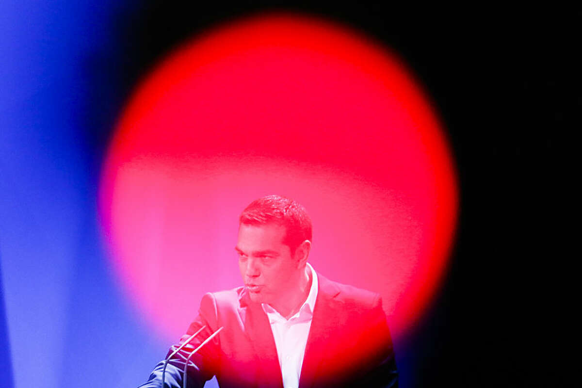 In this photo taken with a red television camera control light in the foreground, the Prime Minister of Greece Alexis Tsipras briefs the media on a news conference during a bilateral meeting with German Chancellor Angela Merkel at the chancellery in Berlin, Monday, March 23, 2015. (AP Photo/Markus Schreiber)