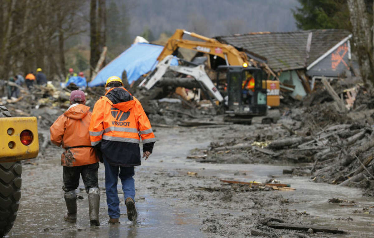 Workers walk through mud as heavy equipment operators work to clear debris Tuesday, March 25, 2014, from Washington Highway 530 on the western edge of the massive mudslide that struck the area Saturday, killing at least 14 people and leaving dozens missing. (AP Photo/Ted S. Warren, Pool)