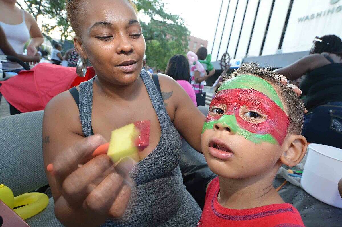 Hour Photo/Alex von Kleydorff Shalonda Candelabio puts the final touches on a teenage mutant Ninja Turtle mask for 4 yr old Tre'vone Peterson during a Community Summer Mixer sponsored by GGP, to let people know about the proposed mall for South Norwalk. Residents were treated to free hot dogs hamburgers and all the trimmings and were entertained by a DJ, face painting and a balloon artist in the plaza at 50 Washington st.