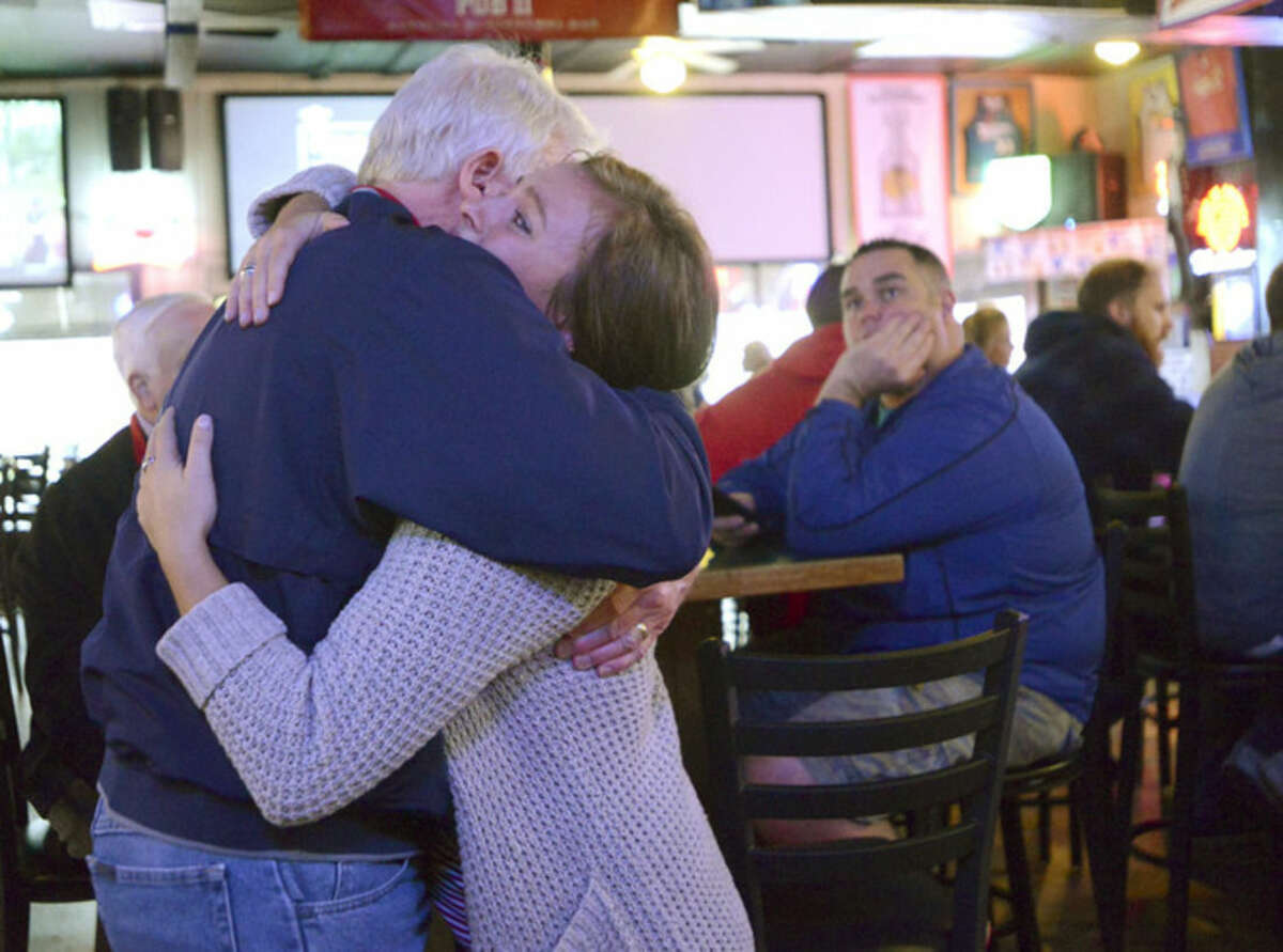 Pub II waitress Maddie DeGaealu and long time customer and friend Ken Hoffacker embrace while comforting each other in the Normal, Ill., bar, after learning that co-owner Terry Stralow is one of seven killed in the crash of a small aircraft east of Bloomington, Ill., Tuesday, April 7, 2015. (AP Photo/The Pantagraph, Steve Smedley)