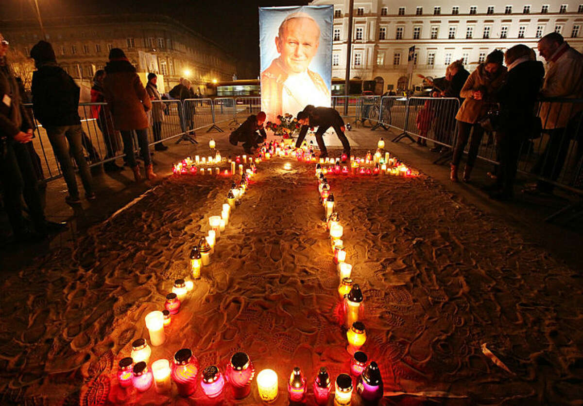 People pray and light candles before a portrait of Polish-born Pope John Paul II in Warsaw, Poland, on Wednesday, April 2, 2014 to mark nine years since the death of the much-loved pontiff who will be made a saint in a Vatican ceremony on April 27. (AP Photo/Czarek Sokolowski)