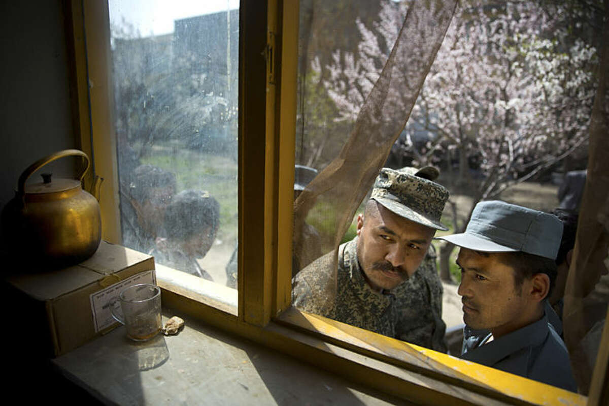 An Afghan soldier, left, and a police man peek through a window as they queue with others to get their registration card on the last day of voter registration for the upcoming presidential elections outside a school in Kabul, Afghanistan, Tuesday, April 1, 2014. Elections will take place on April 5, 2014. (AP Photo/Anja Niedringhaus)