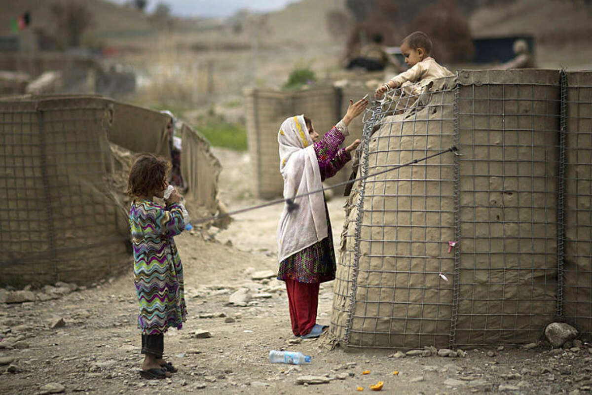 An Afghan girl helps her brother down from a security barrier set up outside the Independent Election Commission (IEC) office in the eastern Afghan city of Khost, Thursday, April 3, 2014. Afghans go to the polls to elect a new President on April 5, 2014. (AP Photo/Anja Niedringhaus)