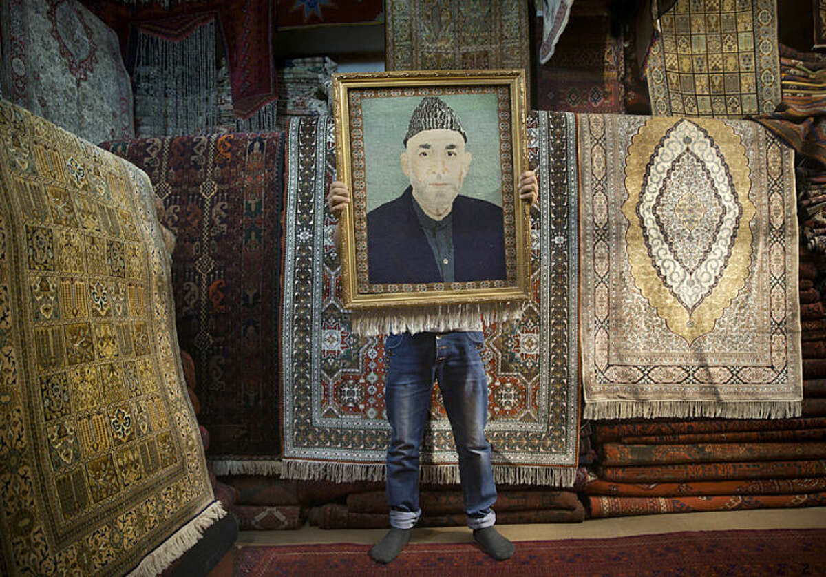 FILE - In this Sunday, March 30, 2014 file photo, an Afghan carpet seller holds up a framed carpet depicting Afghan President Hamid Karzai in his store in Kabul, Afghanistan. Anja Niedringhaus, a courageous and immensely talented Associated Press photographer who has covered everything from sports to war, was killed while covering elections in Afghanistan on Friday April 4, 2014. Niedringhaus was in a car in eastern Afghanistan with AP reporter Kathy Gannon when, according to a freelancer who was with them, an Afghan policeman approached them, yelled "Allahu Akbar" - God is Great -and opened fire on them in the back seat with his AK-47. Niedringhaus was killed instantly and Gannon was wounded. (AP Photo/Anja Niedringhaus, File)