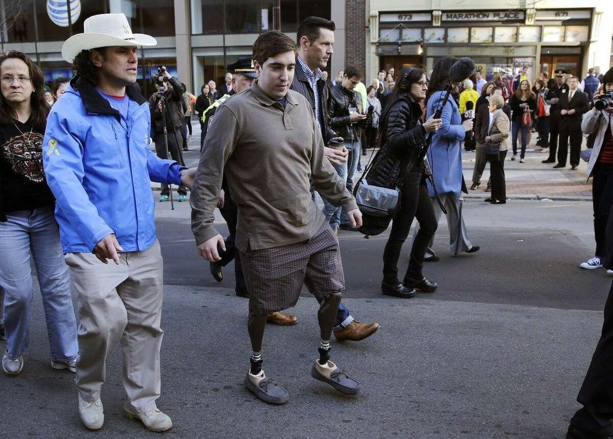 Boston Marathon survivor Jeff Bauman, right, walks past one of two blast sites with Carlos Arredondo, who helped save his life, near the finish line of the Boston Mararthon in Boston, Wednesday, April 15, 2015. Boston marked the second anniversary of the 2013 marathon bombings with a subdued remembrance that includes a moment of silence, the pealing of church bells and a call for kindness. (AP Photo/Charles Krupa)