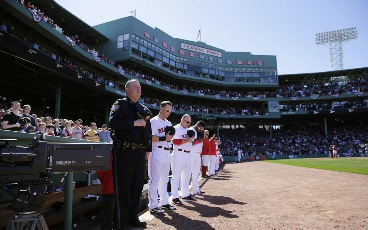 Boston Red Sox players, fans and a Boston Police officer pause for a moment of silence at 2:49pm, the time of the first bomb explosion near the finish line of the Boston Marathon in 2013, at the start of the fourth inning of a baseball game against the Washington Nationals at Fenway Park in Boston, Wednesday, April 15, 2015. Boston marked the second anniversary of the bombings with a subdued remembrance that includes a moment of silence, the pealing of church bells and a call for kindness. (AP Photo/Charles Krupa)