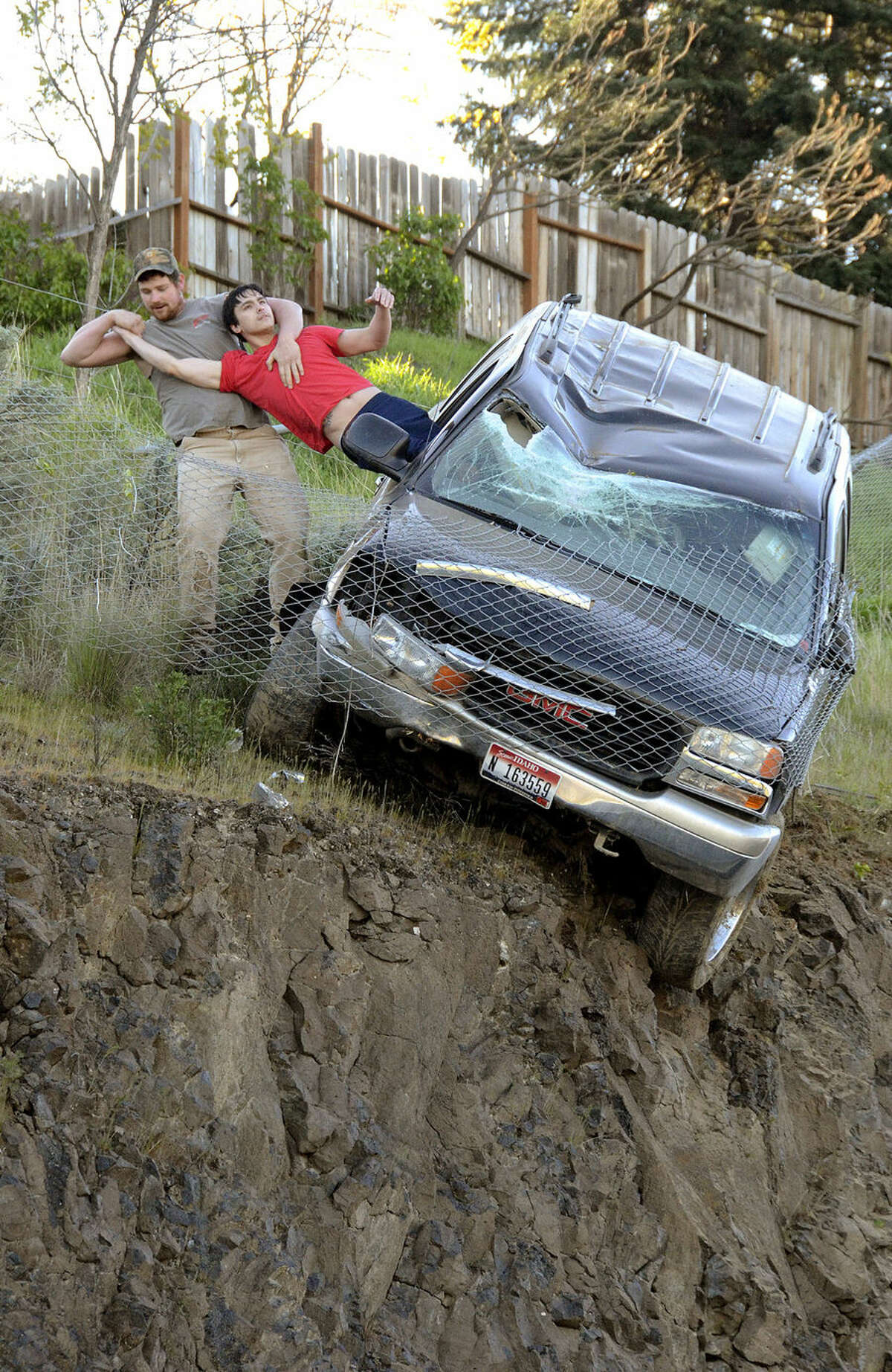 An unidentified passer-by pulls the driver from a SUV to safety after the vehicle left Mayfair Drive, traveled downhill and was stopped by a chain link fence just short of a 30-foot vertical drop onto the Bryden Canyon Road, Wednesday, April 15, 2015, in Lewiston, Idaho. (Barry Kough/Lewiston Tribune via AP)