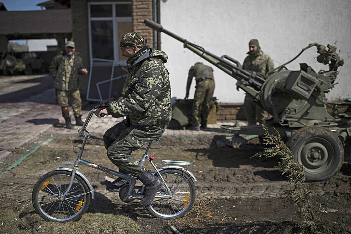 A Ukrainian serviceman rides a bicycle in Shyrokyne, eastern Ukraine, Wednesday, April 15, 2015. Russia and Ukraine agreed in Berlin on Monday to call for the pullback of smaller-caliber weapons from the front lines of the conflict that has claimed more than 6,000 lives. (AP Photo/Evgeniy Maloletka)