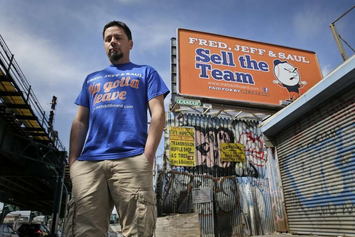 Gary Palumbo poses for a picture next to a billboard criticizing the ownership of the New York Mets across the street from Citi Field, Monday, April 13, 2015 in New York. Palumbo, a 39-year-old Mets fan who lives in New Hampshire, raised $6,700 on Kickstarter and paid for the billboards. (AP Photo/Seth Wenig)