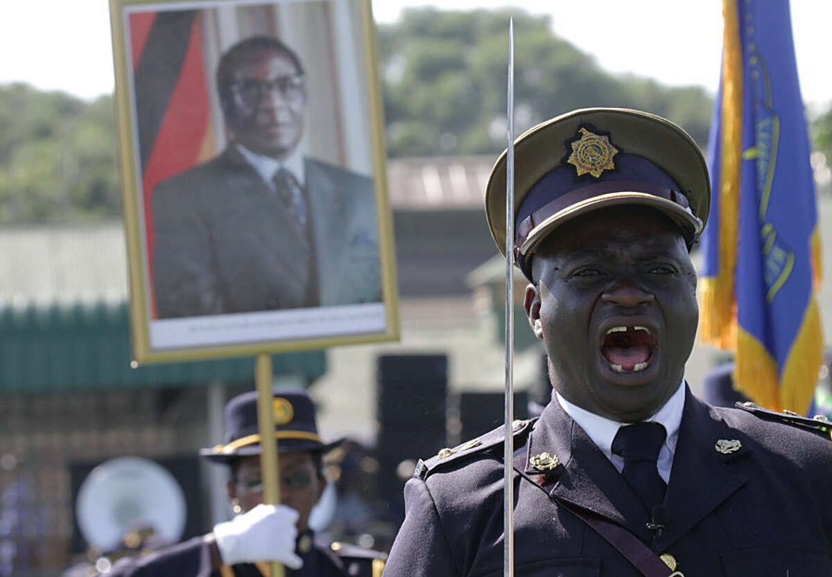 A police officer shouts orders during the Presidential Graduation ceremony which was attended by President Robert Mugabe, pictured in poster in the background, at the General Police headquarters, in Harare, Zimbabwe, Thursday, May 14, 2015. A total of 698 police officers graduated at the ceremony after undergoing training by the Zimbabwe Republic police. (AP Photo/Tsvangirayi Mukwazhi)