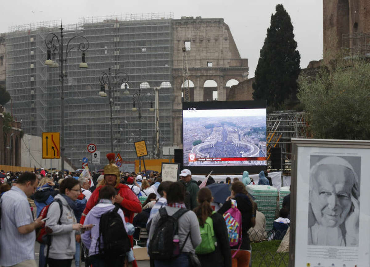 People follow the ceremony for the canonizations of Pope John XXIII and Pope John Paul II taking place at the Vatican on giant screens set up at the Colosseum, in Rome, Sunday, April 27, 2014. Pope Francis declared Popes John XXIII and John Paul II (on a large drawing at right) saints before some 800,000 people on Sunday in an unprecedented ceremony.(AP Photo/Riccardo De Luca)