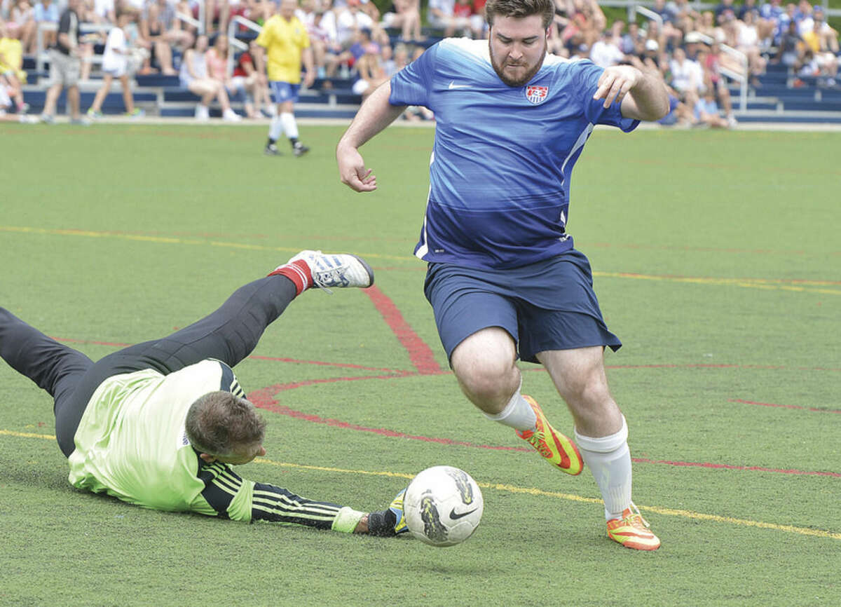 Hour photo/Alex von Kleydorff Wilton Blue's Tom Conley, right, gets past the Ancient Warriors' goalie on his way to scoring a goal during Monday's game in the ninth annual Memorial Soccer Challenge event at Lilly Field in Wilton.