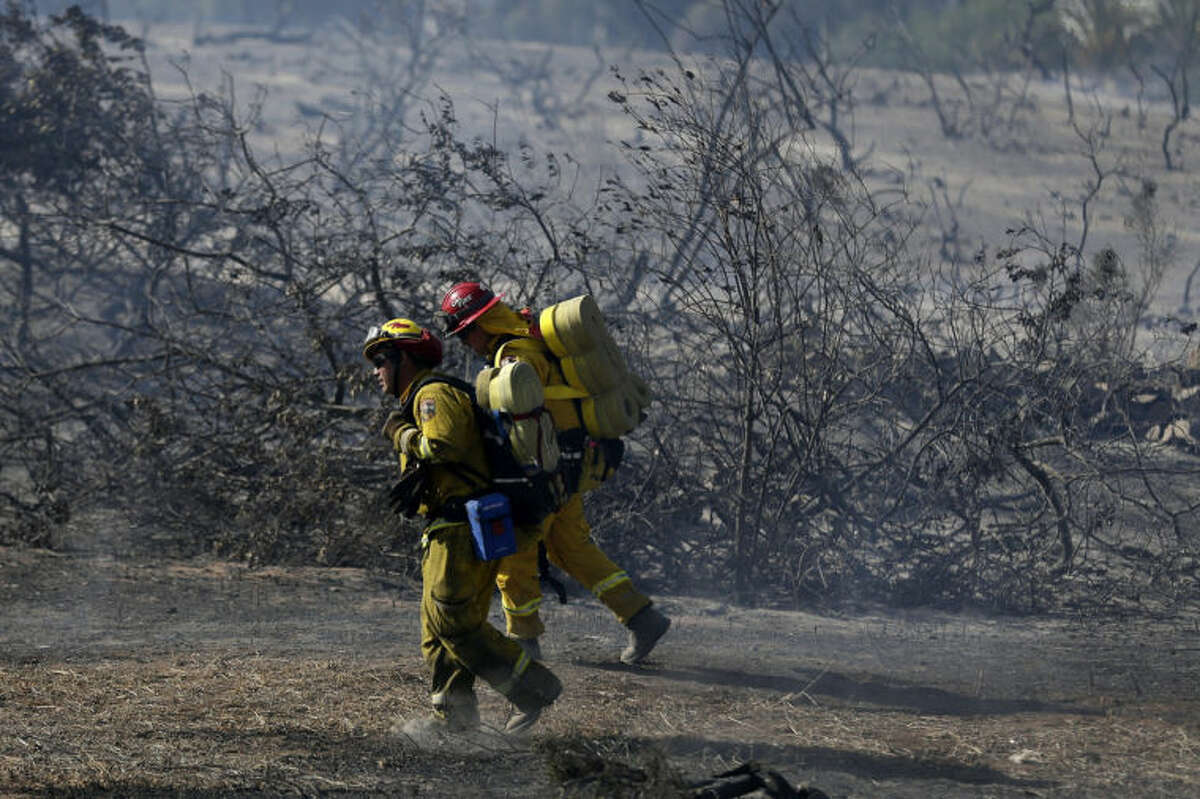 Firefighters make hike through burned vegetation during a wildfire Wednesday, May 14, 2014, in Carlsbad, Calif. Flames engulfed suburban homes and shot up along canyon ridges in one of the worst of several blazes that broke out Wednesday in Southern California during a second day of a sweltering heat wave, taxing fire crews who fear the scattered fires mark only the beginning of a long wildfire season. (AP Photo)