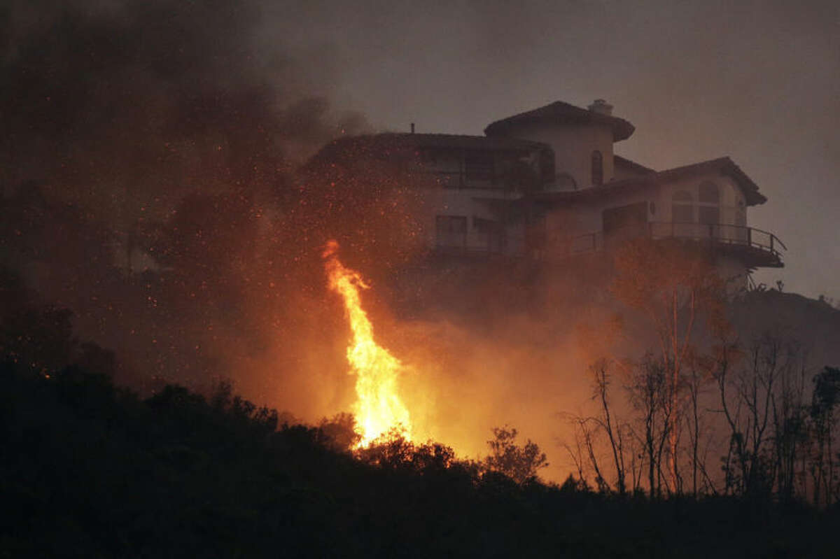 A wildfire burns near a home on Wednesday, May 14, 2014, in San Marcos, Calif. Flames engulfed suburban homes and shot up along canyon ridges in one of the worst of several blazes that broke out Wednesday in Southern California during a second day of a sweltering heat wave, taxing fire crews who fear the scattered fires mark only the beginning of a long wildfire season. (AP Photo)