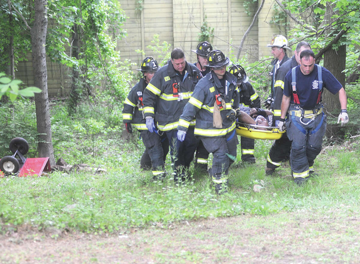 First responders pull a man up the hill at Crossland Place in Norwalk Tuesday afternoon when his lawn tractor slid down a hill and landed on top of him. Hour photo/Matthew Vinci