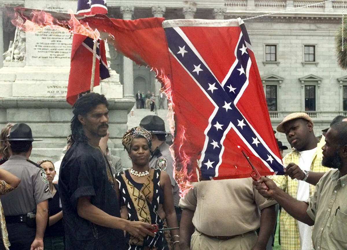 FILE - In this Wednesday, May 10, 2000 file photo, Kevin Gray, of the Harriett Tubman Freedom House, watches as the Confederate flag burns during a demonstration in Columbia, S.C., to protest the Confederate flag flying atop the dome of the South Carolina Statehouse. On the left side was a Nazi flag which burned first. (AP Photo/Lou Krasky)