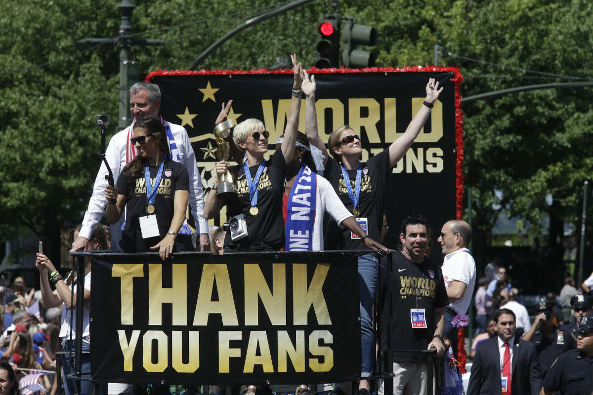 U.S. women's soccer team midfielder Megan Rapinoe, center, holds up the World Cup trophy as midfielder Carli Lloyd, left, New York City Mayor Bill de Blasio, left background, and head coach Jill Ellis, right, wave to the crowd as their float makes it way up Broadway's Canyon of Heroes during the ticker tape parade to celebrate the U.S. women's soccer team World Cup victory, Friday, July 10, 2015, in New York. (AP Photo/Mary Altaffer)