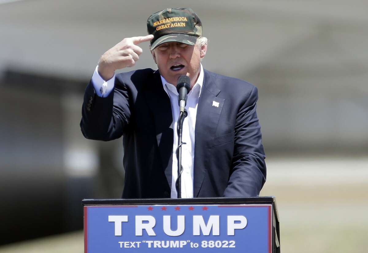 In this June 3, 2016, photo, Republican presidential candidate Donald Trump gestures to a his camouflaged "Make America Great" hat as he discuses his support by the National Rifle Association at a campaign rally at the Redding Municipal Airport in Redding, Calif.