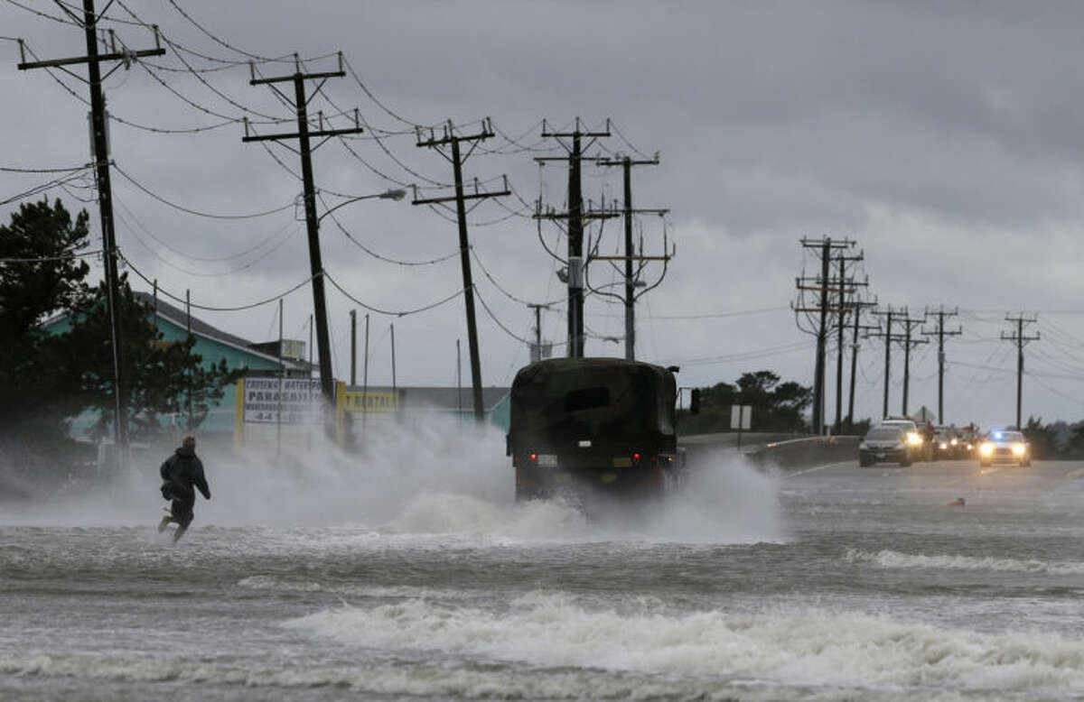 A military vehicle and a man navigate a flooded Highway 64 as wind pushes water over the road while Hurricane Arthur passes through Nags Head, N.C., Friday, July 4, 2014. (AP Photo/Gerry Broome)