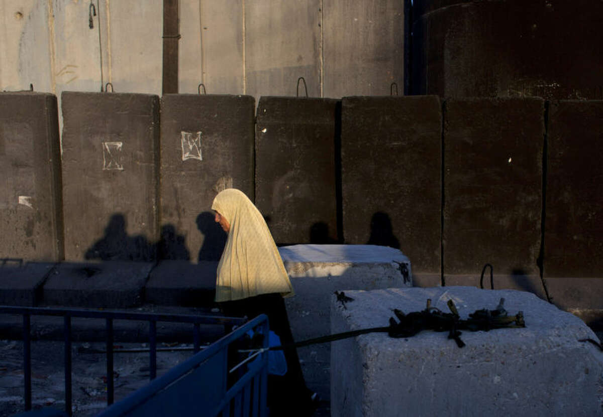 A Palestinian woman walks by the Israeli separation barrier on her way to Jerusalem through the Qalandia security checkpoint, on the outskirts of the West Bank city of Ramallah, Friday, July 4, 2014. (AP Photo/Nasser Nasser)