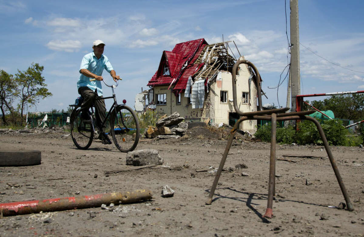 A man rides a bike past a house damaged during fighting, outside the city of Slovyansk, Donetsk Region, eastern Ukraine Thursday, July 10, 2014. In the past two weeks, Ukrainian government troops have halved the amount of territory held by the rebels. Now they are vowing a blockade of Donetsk. In another sign of deteriorating morale among rebels, several dozen militia fighters in Donetsk abandoned their weapons and fatigues Thursday, telling their superiors they were returning home. (AP Photo/Dmitry Lovetsky)