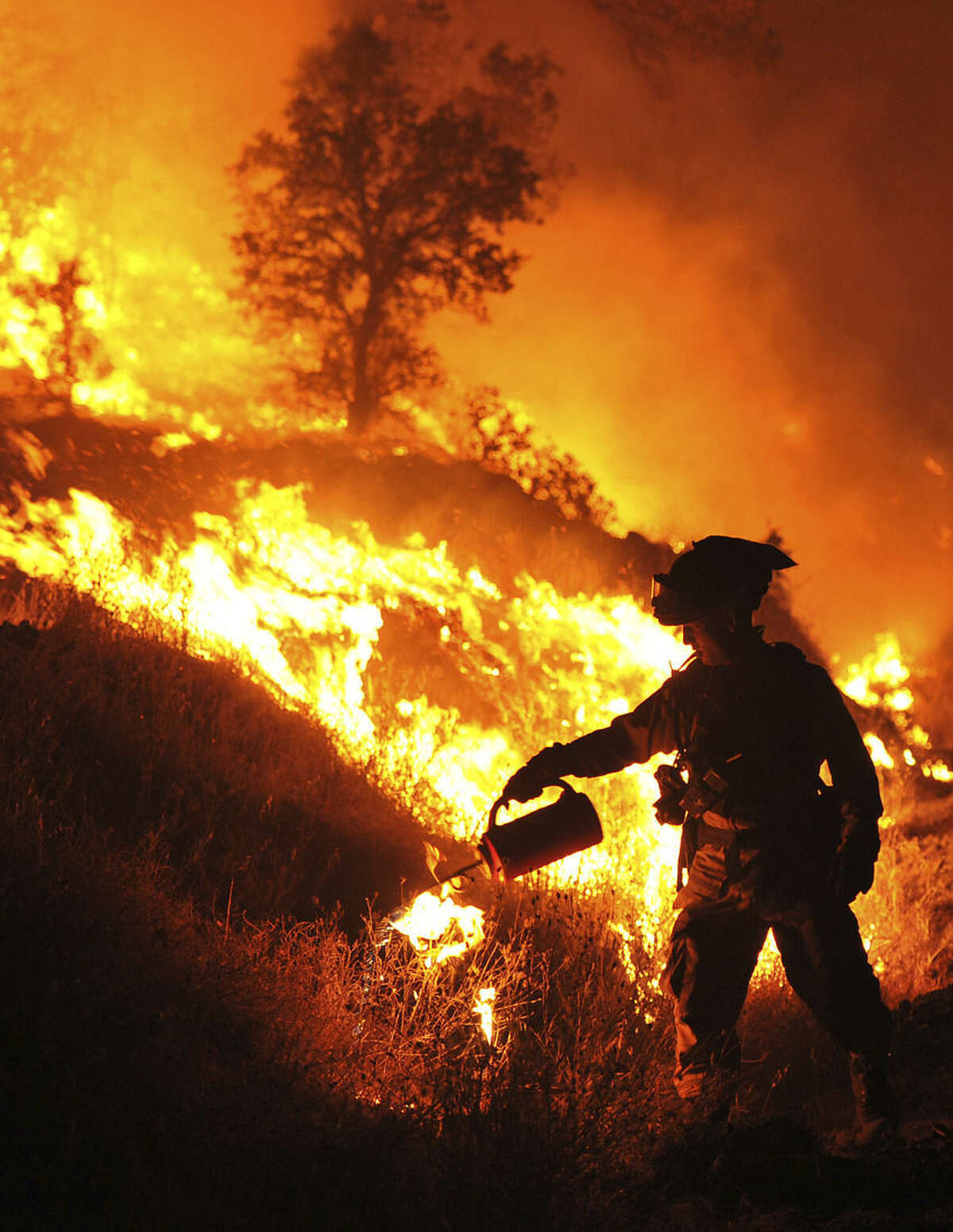 CalFire firefighter Bo Santiago lights a backfire as the Rocky Fire burns near Clearlake, Calif., on Monday, Aug. 3, 2015. The fire has charred more than 60,000 acres and destroyed at least 24 residences. (AP Photo/Josh Edelson)