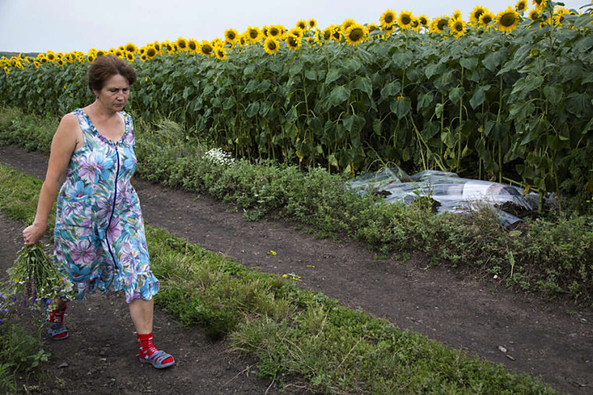 A woman walks past a body covered with a plastic sheet near the site of a crashed Malaysia Airlines passenger plane near the village of Rozsypne, Ukraine, eastern Ukraine Friday, July 18, 2014. Rescue workers, policemen and even off-duty coal miners were combing a sprawling area in eastern Ukraine near the Russian border where the Malaysian plane ended up in burning pieces Thursday, killing all 298 aboard. (AP Photo/Dmitry Lovetsky)