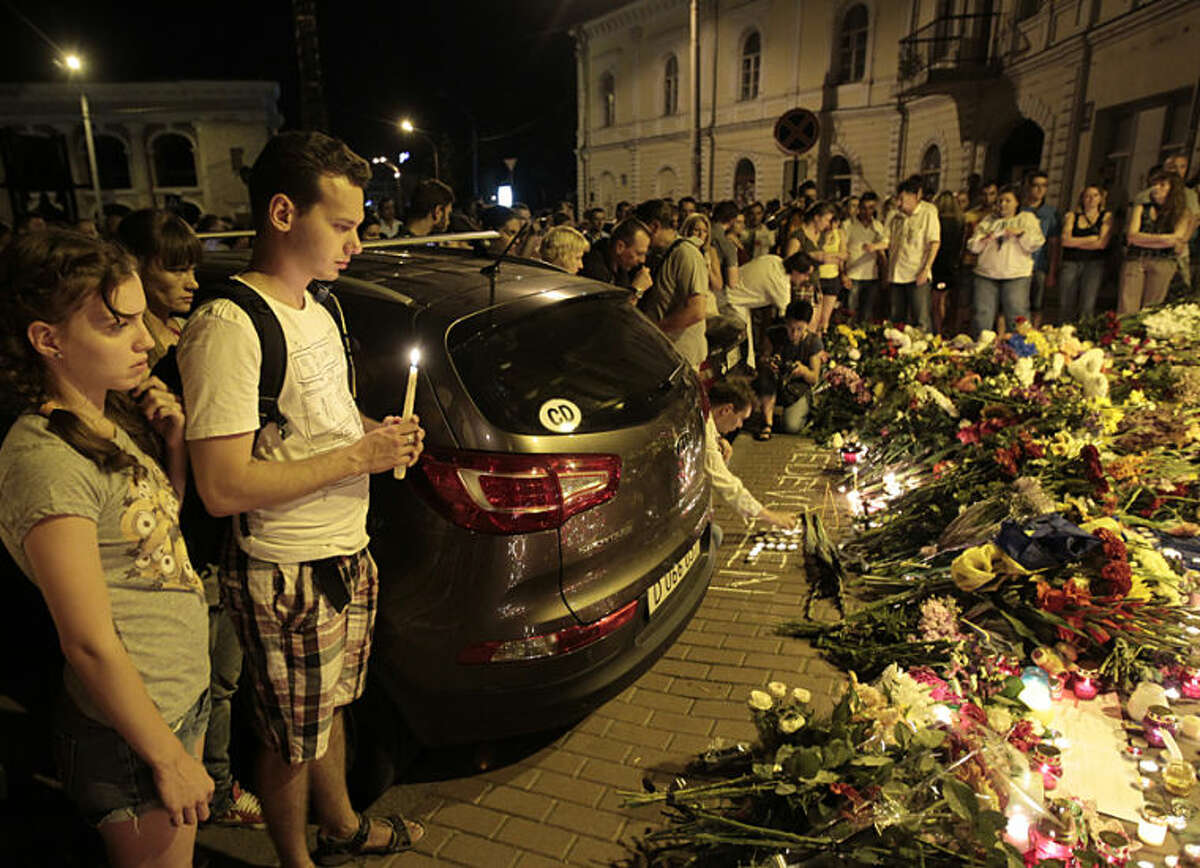 People stand near flower tributes placed outside the Dutch embassy to commemorate victims of Malaysia Airlines plane crash in Kiev, Ukraine, Thursday, July 17, 2014. A Malaysian Airlines passenger jet was shot down in eastern Ukraine on Thursday, and both the Ukrainian government and pro-Russian rebels blamed one another for the attack.(AP Photo/Sergei Chuzavkov)