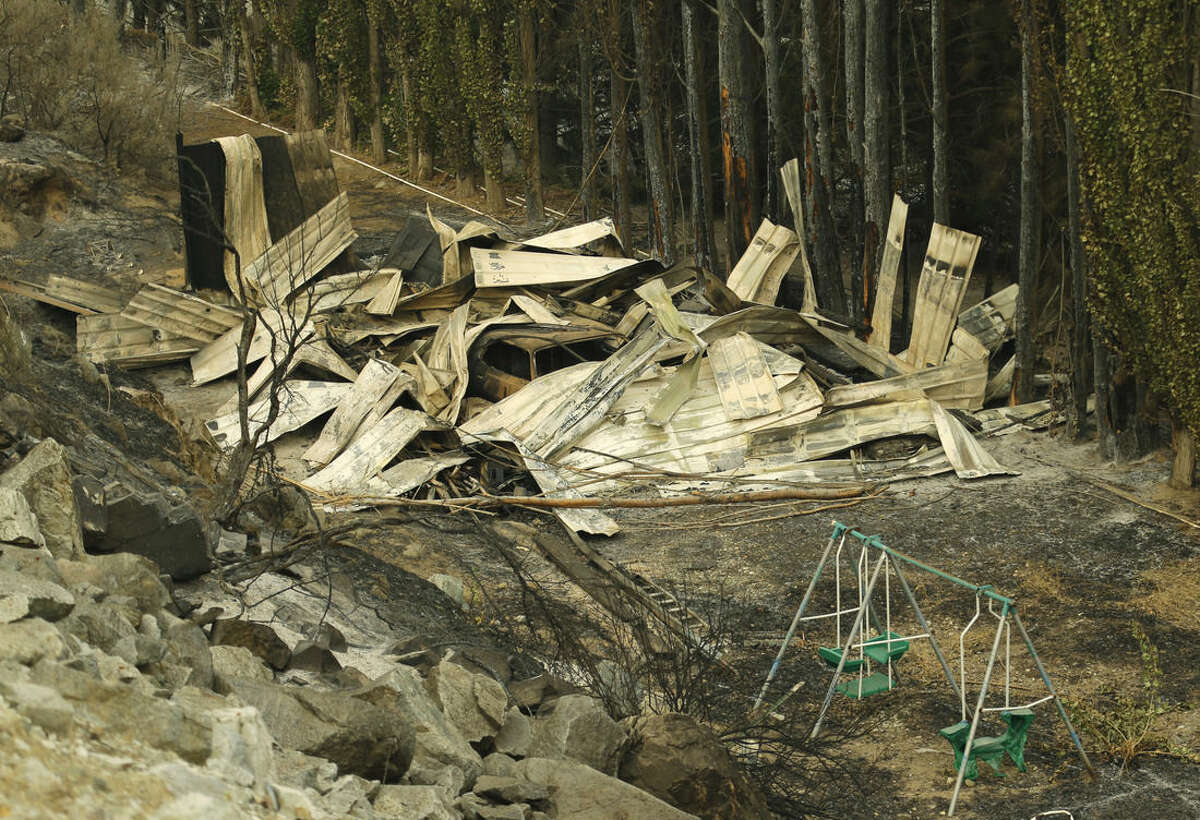 A partially melted swing set sits next to a burned structure along State Route Alt. 97 highway Monday, Aug. 17, 2015, outside of Chelan, Wash. The blazes near Chelan, about 180 miles east of Seattle, are burning through grass, brush and timber, fire spokeswoman Janet Pearce said. (AP Photo/Ted S. Warren)