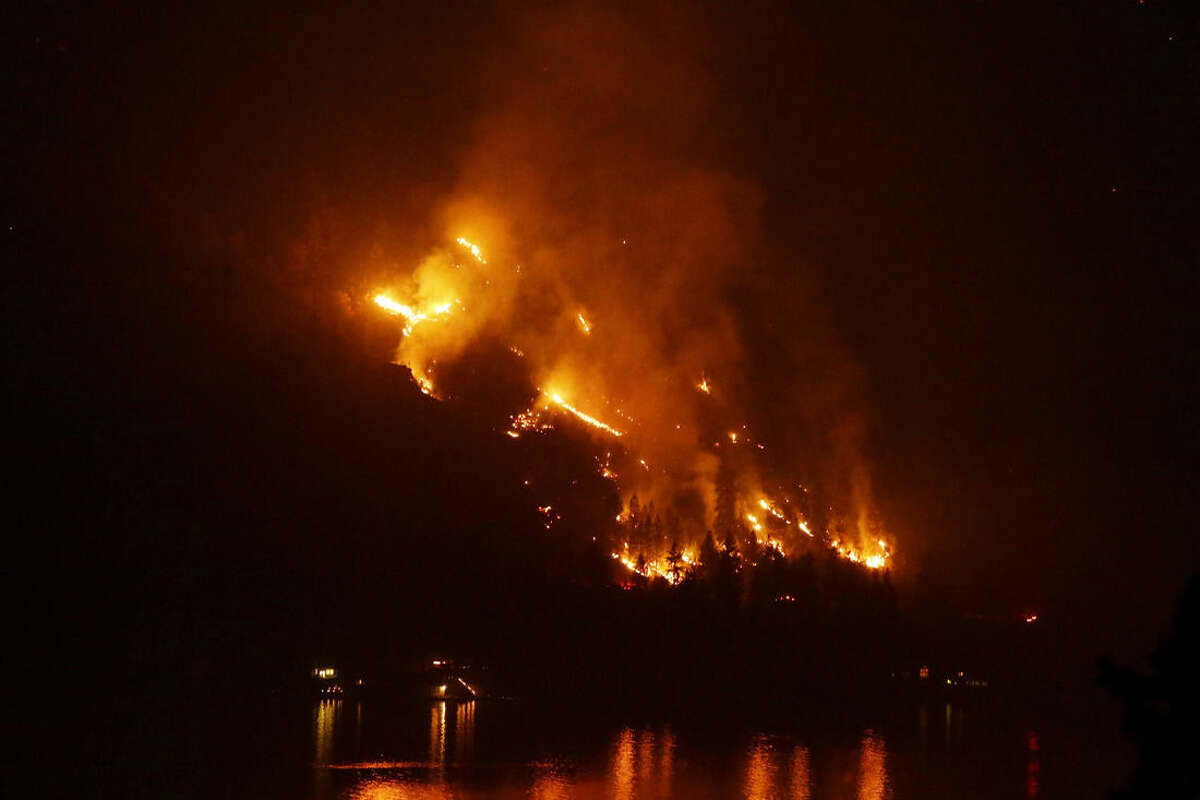 Timber burns in the First Creek fire near lakeside structures on the western shore of Lake Chelan late Monday, Aug. 17, 2015, near Chelan, Wash. Big wildfires threatened the Lake Chelan resort region of central Washington on Monday after driving away tourists, destroying a warehouse filled with nearly 2 million pounds of apples and forcing thousands of residents to flee. (AP Photo/Ted S. Warren)