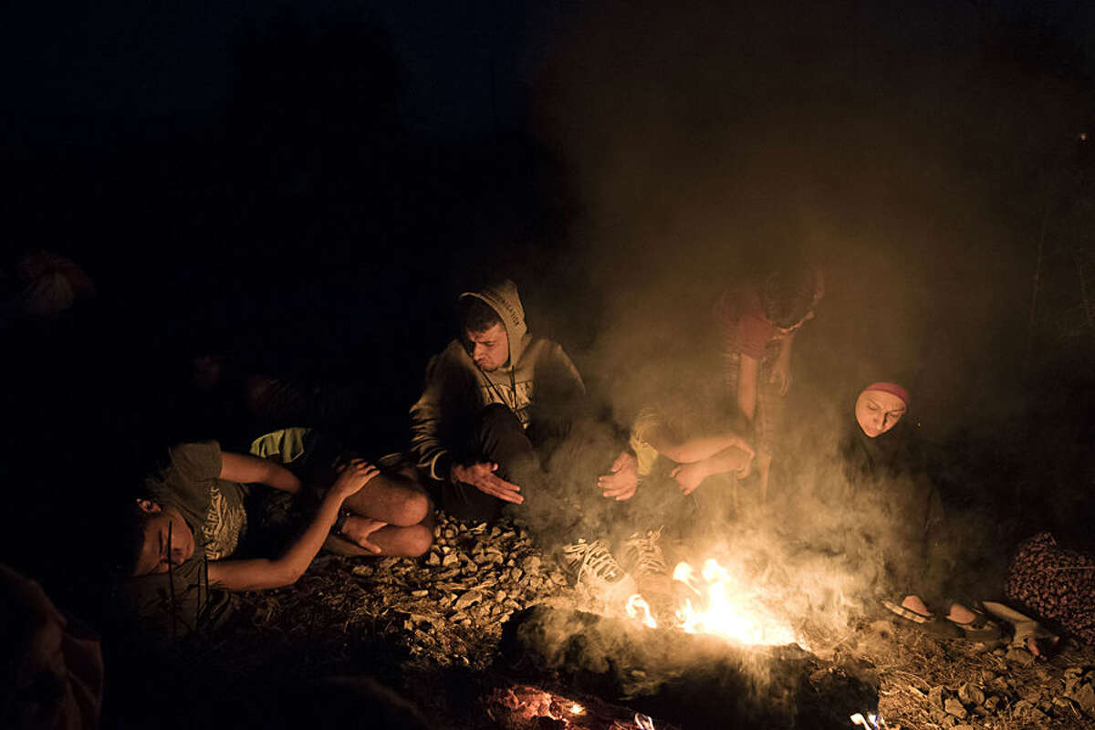 Syrian refugees warm up near fire as they wait near the border train station of Idomeni, northern Greece, to be allowed by the Macedonian police to cross the border from Greece to Macedonia, Tuesday, Aug. 18, 2015. More than 135,000 migrants have arrived on Greek islands so far this year, hoping to head north to other more prosperous European countries such as Germany, the Netherlands and Scandinavian countries. (AP Photo/Giannis Papanikos)
