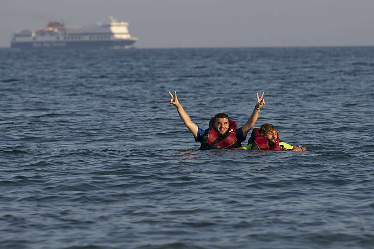 Two Syrian refugees gesture as they swim from their boat after crossing from Turkey, at the southeastern island of Kos, Greece, early Monday, Aug. 17, 2015. With the lights of the Greek island of Kos twinkling through the darkness, beacons of hope for a new and better life, another group of migrants has come through this wealthy tourist town to make a risky, but less risky than most, sea crossing and apply for asylum in Europe. (AP Photo/Alexander Zemlianichenko)