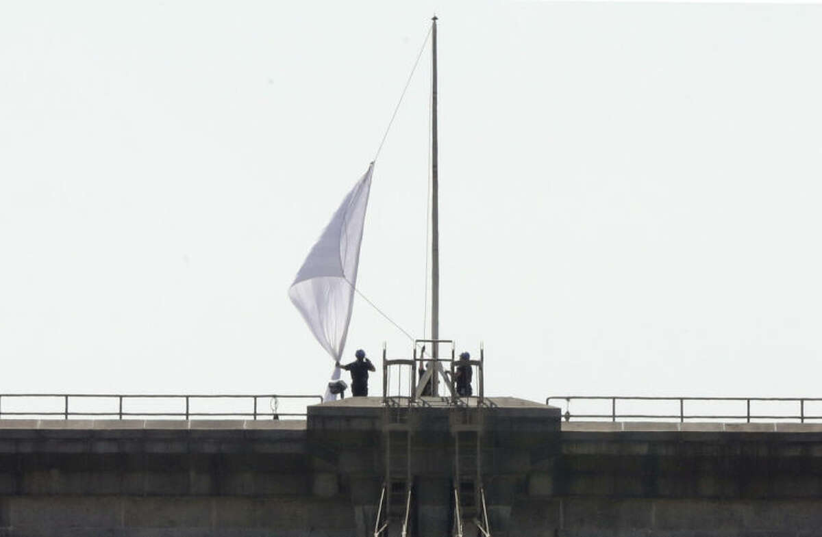 New York City Police officers lower a white flag flying atop the west tower of New York's Brooklyn Bridge, Tuesday, July 22, 2014. Someone replaced two American flags on the bridge with mysterious white flags. The white flags, international symbols of surrender, fluttered from poles on the stone supports that hold cables above the bridge connecting Brooklyn and Manhattan. An entity called Bike Lobby tweeted Tuesday that it hoisted the flags to signal ?“surrender of the Brooklyn Bridge bicycle path to pedestrians.?” (AP Photo/Richard Drew)