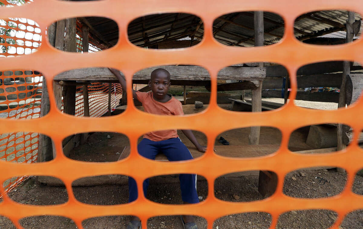 In this photo taken Friday, Aug. 14, 2015, a child waits to be released from quarantine as police officers stand guard while people dance while they are finally released from Ebola quarantine by Sierra Leone President Ernest Bai Koroma, in the village of Massessehbeh on the outskirts of Freetown, Sierra Leone. Five long months after a man traveled to his hometown for festivities marking the end of Ramadan, and died suddenly from Ebola, President Koroma has come to cut down the fencing to mark the formal end of Sierra Leone's largest remaining Ebola quarantine. (AP Photo/Sunday Alamba)