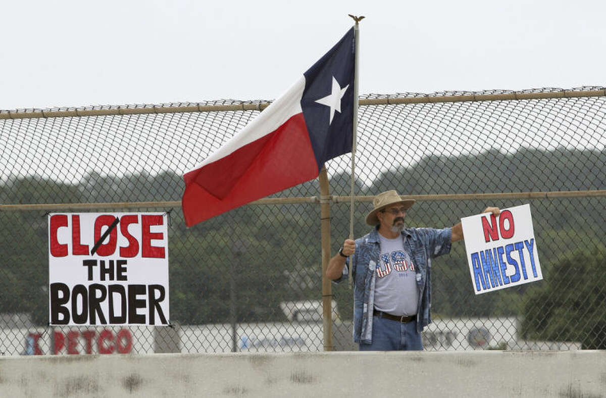 A protester waves a Texas flag and anti-immigration signs during a protest against people who immigrate illegally, Saturday, July 19, 2014, in Conroe, Texas. Texas Gov. Rick Perry took his border security criticisms to an audience of Hispanic ministers in San Antonio, telling them the federal government should put more Border Patrol troops on the ground and drones in the air to secure the Texas-Mexico border. (AP Photo/Conroe Courier, Jason Fochtman)