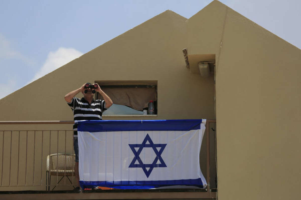 FILE - In this Monday, July 21, 2014 file photo, a man uses binoculars to look at the Gaza Strip from his balcony in the town of Sderot, Israel after a group of Hamas militants was detected infiltrating into Israel. With deadly fighting raging next door in the Gaza Strip, southern Israeli towns along the border have turned into mini army bases as most residents have fled. (AP Photo/Tsafrir Abayov, File)
