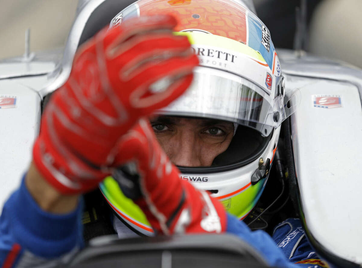 FILE - This is a May 14, 2015, file photo showing Justin Wilson, of England, putting on his gloves as he prepares to drive during practice for the Indianapolis 500 auto race at Indianapolis Motor Speedway in Indianapolis. The British driver was in a coma in critical condition after sustaining a head injury when he was hit by a large piece of debris that broke off another car in the crash-filled race at Pocono Raceway on Sunday, Aug. 23, 2015. (AP Photo/Michael Conroy, File)