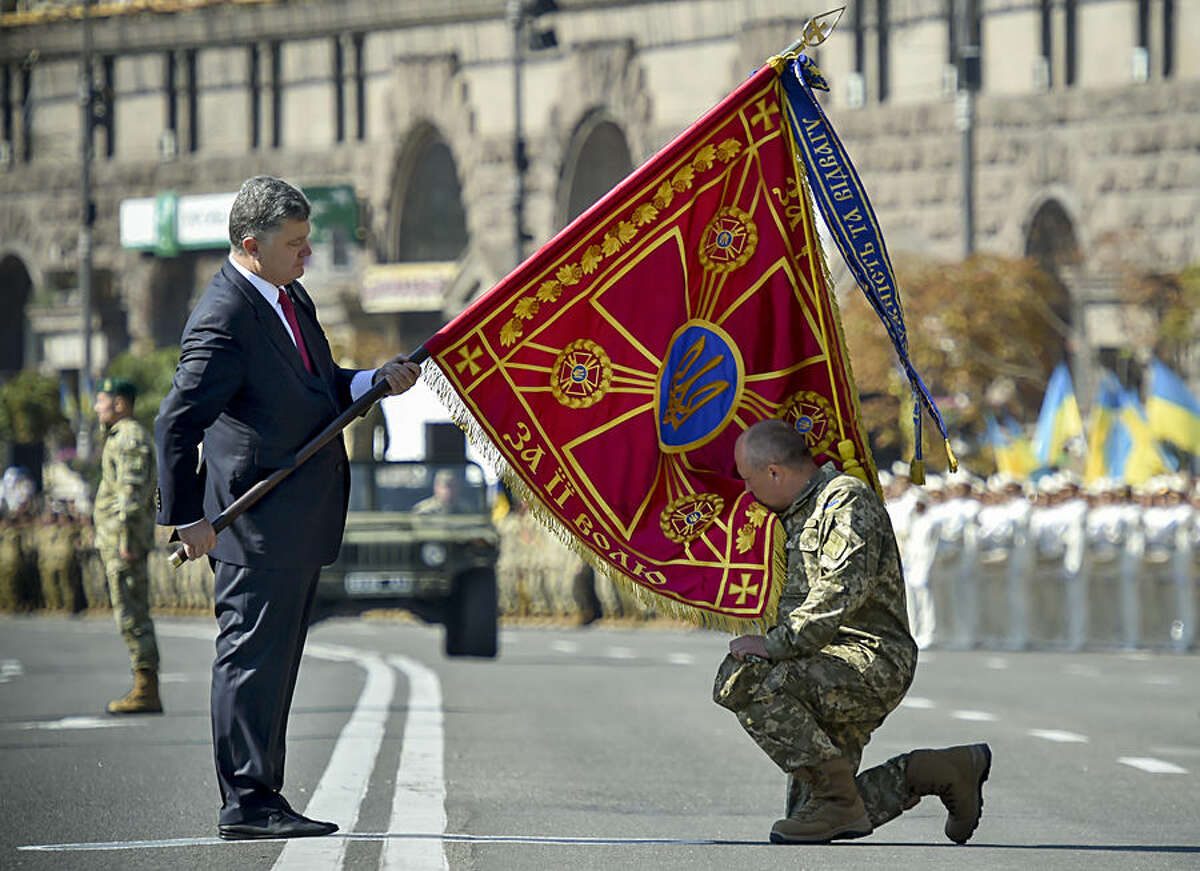 Ukraine's President Petro Poroshenko hands over a flag of a military unit as a soldier kisses the flag before a military parade on the occasion of Ukraine's Independence Day in the capital Kiev, Ukraine, Monday, Aug. 24, 2015. Speaking at the parade, President Petro Poroshenko said Ukraine would continue to increase its troop numbers in order to fend off the attacks of separatist rebels.(AP Photo/Mykola Lazarenko, Pool)