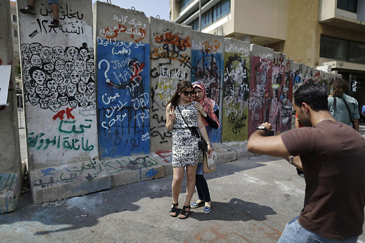 Lebanese women have their picture taken in front a concrete wall installed by authorities near the main Lebanese government building, in downtown Beirut, Lebanon, Tuesday, Aug. 25, 2015. Anticipating more protests, authorities installed a concrete wall near the main Lebanese government building, site of the largest protests. On Saturday and Sunday nights, police fired tear gas and water cannons at the protesters, battling them in the streets of Beirut in dramatic clashes, wounding dozens. (AP Photo/Hassan Ammar)
