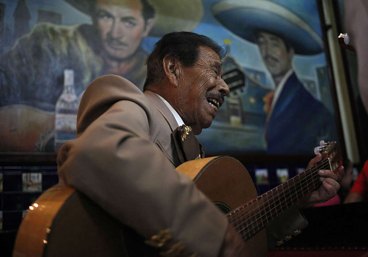 In this July 29, 2015 photo, 90-year-old mariachi Jose Jesus performs inside the Salon Tenampa bar and restaurant in Garibaldi Plaza in Mexico City. The mural features late Mexican mariachi legends Pedro Infante, left, and Javier Solis. (AP Photo/Sofia Jaramillo)